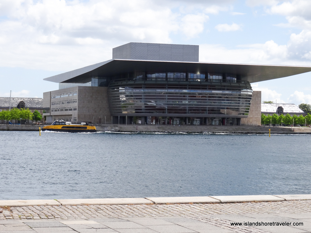Modern concrete and glass structure that is the Royal Danish Opera House with water in the foreground